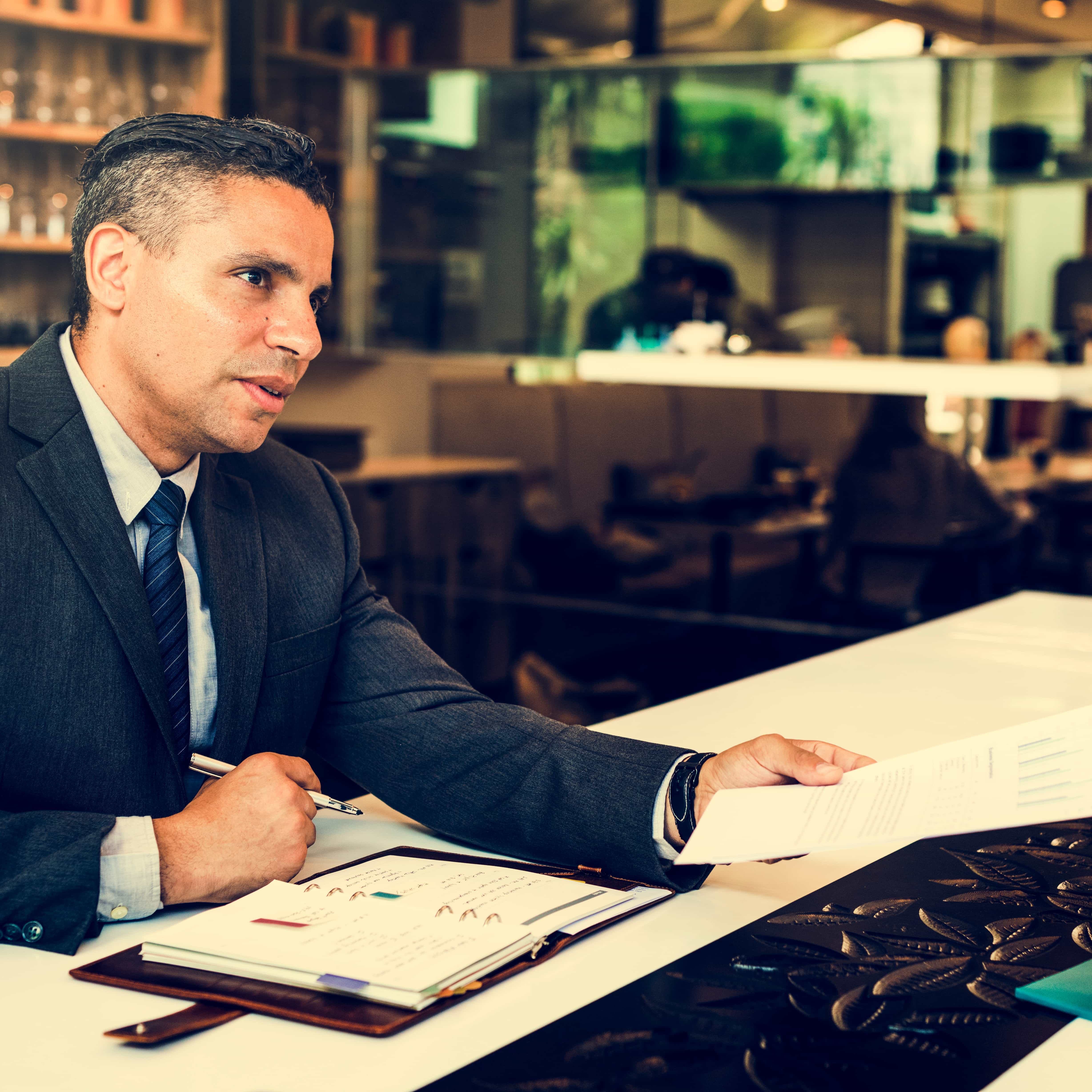 Experto bancario en Cádiz asesorando a un cliente en una oficina moderna, gráficos de finanzas y documentos sobre la mesa